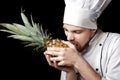 Young bearded man chef In white uniform holds Fresh pineapple on black background Royalty Free Stock Photo