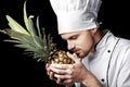 Young bearded man chef In white uniform holds Fresh pineapple on black background Royalty Free Stock Photo
