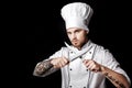 Young bearded man chef In white uniform holds Two knives on black background Royalty Free Stock Photo