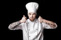 Young bearded man chef In white uniform holds Two knives on black background Royalty Free Stock Photo