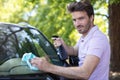 young bearded man cleaning car with cloth