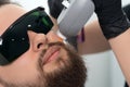 Young bearded man getting laser facial treatment by professional cosmetologist in a beauty clinic. Healthy man lifestyle