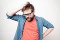 Young bearded man with glasses is in doubt, he is confused, looks down thoughtfully and scratches his head, on a white background