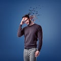 A young bearded man in glasses stands with his head on his forehead while several large pieces fly away from his head. Royalty Free Stock Photo