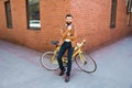 Young bearded man holding hand on chin and looking at camera while sitting near his bicycle outdoors near brick wall Royalty Free Stock Photo