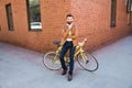 Young bearded man holding hand on chin and looking at camera while sitting near his bicycle outdoors near brick wall Royalty Free Stock Photo