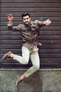 Young bearded man jumping in urban background with open arms wearing casual clothes. Royalty Free Stock Photo