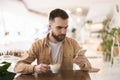 Young bearded man looks serious while checking news in his smartphone during his morning coffee at the cafe, everyday routine