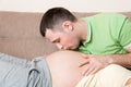 Young bearded man putting his ear close to his pregnant wifes abdomen and kissing it