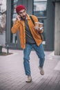 Young bearded man in a red hat talking on the phone and dropping the coffee cups