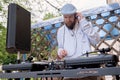 Young bearded man in a shirt and a cap stands behind a dj console in headphones