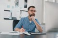 Young bearded man sits in office holding hand near face while working on business project looks busy, takes notes to his Royalty Free Stock Photo