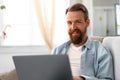 Young bearded man sitting on sofa at home using laptop computer Royalty Free Stock Photo