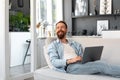 Young bearded man sitting on sofa at home using laptop computer Royalty Free Stock Photo