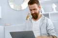 Young bearded man sitting on sofa at home using laptop computer Royalty Free Stock Photo