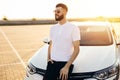 Young bearded man standing near a car outdoors on a summer day, a man in a white shirt stands next to a white car Royalty Free Stock Photo