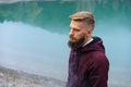 Young bearded man stood alone by lake and looked aside thoughtfully smoking Royalty Free Stock Photo