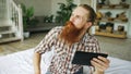 Young bearded man using tablet computer having video chat sitting in bed at home Royalty Free Stock Photo