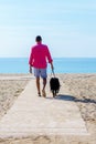 Young bearded man walking with his dog tied up on the beach Royalty Free Stock Photo