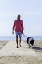 Young bearded man walking with his dog tied up on the beach Royalty Free Stock Photo