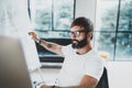 Young bearded man wearing eye glasses and working at sunny office.Blurred background. Horizontal. Cropped.