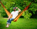 Young bearded man wearing virtual reality goggles relaxing in a garden hammock. Lifestyle VR fun Royalty Free Stock Photo