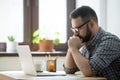 Millennial casual businessman thinking and looking at laptop in Royalty Free Stock Photo