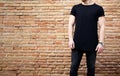 Young bearded muscular man wearing black tshirt and jeans posing outside. Empty brown grunge brick wall on the Royalty Free Stock Photo