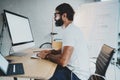 Young bearded professional architect wearing eye glasses working at modern loft studio-office with desktop computer