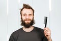 Young bearded shaggy man holding comb. For barbershop