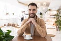 Young bearded smiling man drinks coffee during his lunch break in the cafe, positive vibes