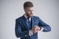 Young bearded stylish businessman leader indoors dressed in three-piece suit checking the time on his watch. isolated on grey Royalty Free Stock Photo