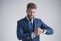 Young bearded stylish businessman leader indoors dressed in three-piece suit checking the time on his watch. isolated on grey Royalty Free Stock Photo