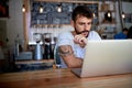 Young bearded tattooed guy in white t-shirt sitting behind the table in bar