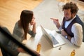 Young beardy caucasian male with curly hair smiling, pointing with index finger at his female colleague. Casual work from home due