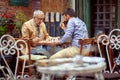 Young beardy guy playing chess with elderly man, sitting in outdoor cafe