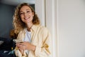 Young beatiful smiling curly woman with phone looking at camera