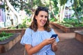 Young beatiful woman smiling happy and cheerful at green park using smartphone on a sunny day of summer Royalty Free Stock Photo