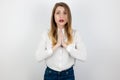 Young beatuiful blond woman standing in praying position, looking innocent on isolated white background , body language concept