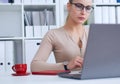 Young beauiful Caucasian businesswoman in glasses working on notebook computer and business document at office.