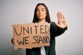 Young beautiful activist asian woman asking unity holding banner with united stand message with open hand doing stop sign with