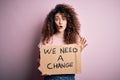 Young beautiful activist woman with curly hair and piercing protesting asking for a change scared in shock with a surprise face,