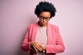 Young beautiful African American afro businesswoman with curly hair wearing pink jacket Checking the time on wrist watch, relaxed Royalty Free Stock Photo