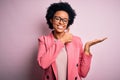 Young beautiful African American afro businesswoman with curly hair wearing pink jacket Showing palm hand and doing ok gesture Royalty Free Stock Photo