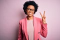 Young beautiful African American afro businesswoman with curly hair wearing pink jacket smiling looking to the camera showing Royalty Free Stock Photo