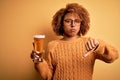 Young beautiful African American afro woman with curly hair drinking glass of beer with angry face, negative sign showing dislike Royalty Free Stock Photo