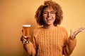 Young beautiful African American afro woman with curly hair drinking glass of beer very happy and excited, winner expression Royalty Free Stock Photo