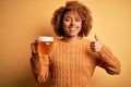 Young beautiful African American afro woman with curly hair drinking jar of beer happy with big smile doing ok sign, thumb up with Royalty Free Stock Photo