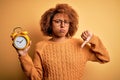 Young beautiful African American afro woman with curly hair holding vintage alarm clock with angry face, negative sign showing Royalty Free Stock Photo