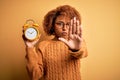 Young beautiful African American afro woman with curly hair holding vintage alarm clock with open hand doing stop sign with Royalty Free Stock Photo